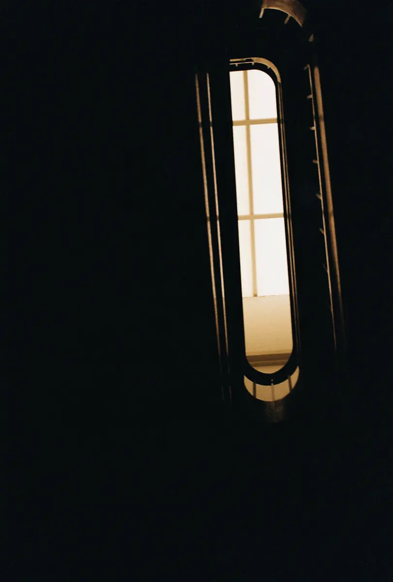 A tall narrow lit window in a dark frame