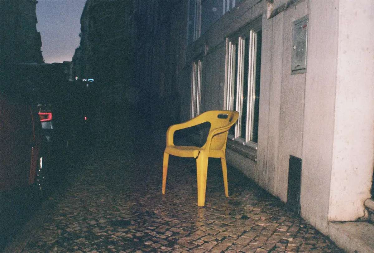 A yellow plastic chair in a dark alley