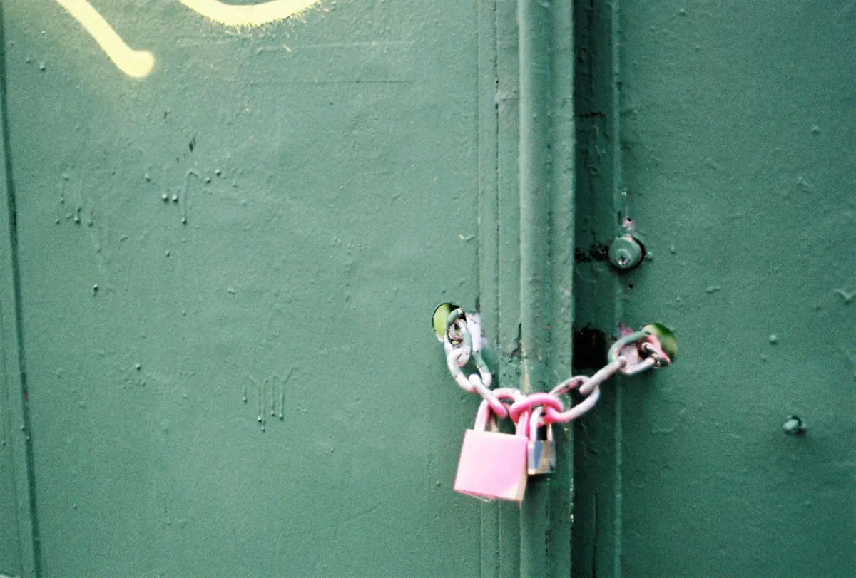 A pink padlock and chain on a green door