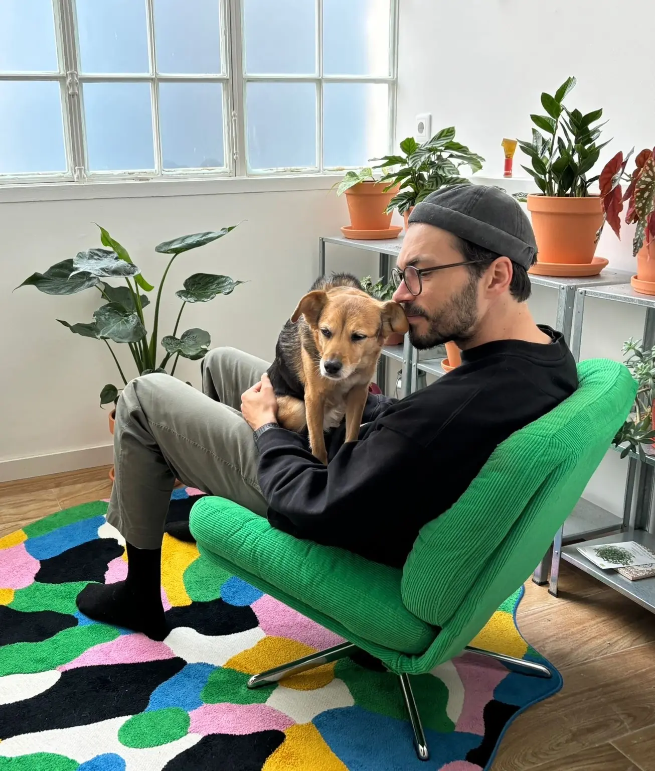 Martin in a beanie and glasses, holding a dog in a green armchair