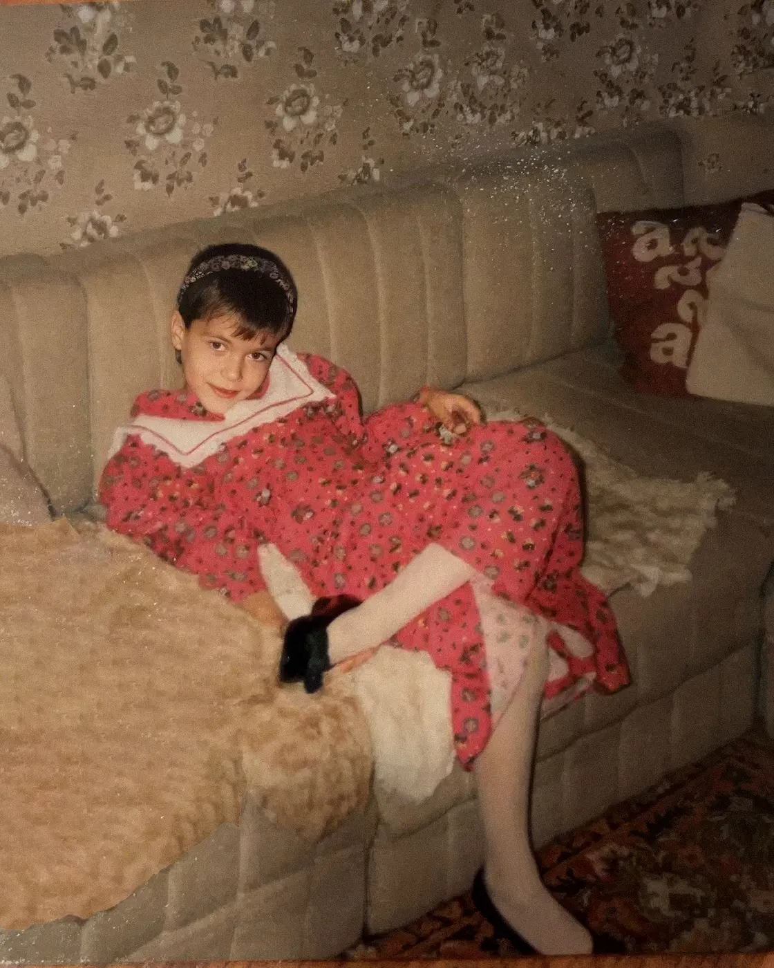 Martin as a child, lying on a sofa in a red dress and a hair band