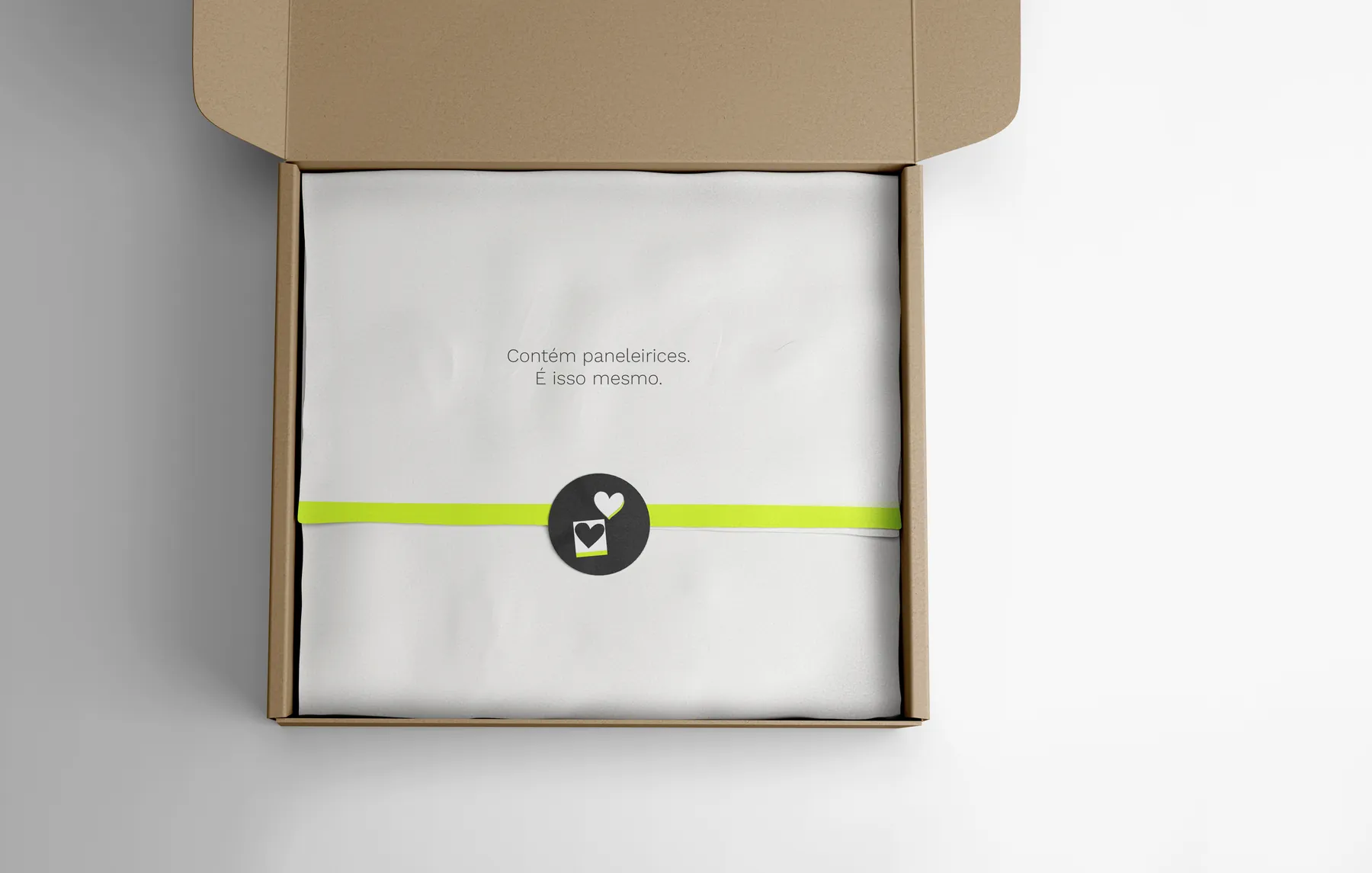 An open shipping box with tissue paper reading Contém paneleirices, sealed with a heart sticker