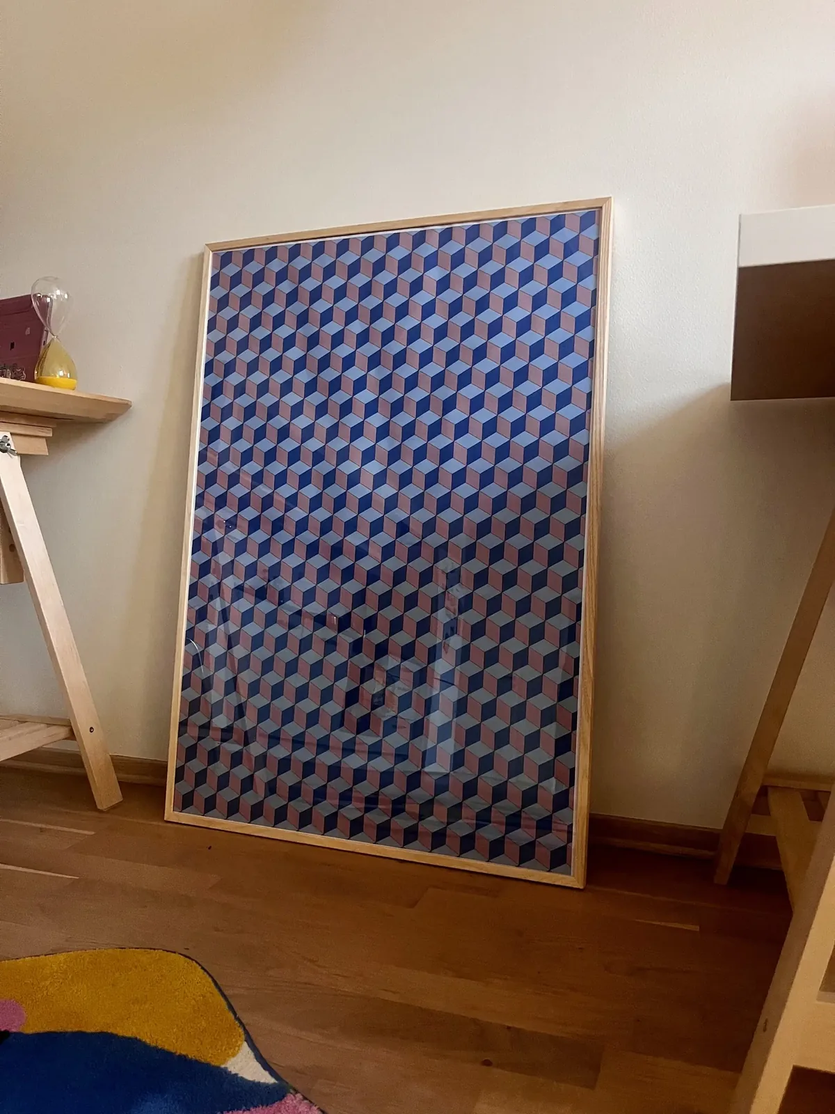Framed rhombille-tiling poster in dusty pink, navy and light blue, leaning against a wall