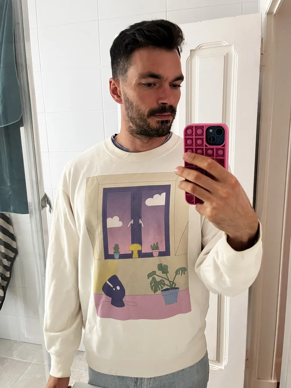 Martin in a mirror selfie wearing a cream sweater with the sunrise illustration printed on the front